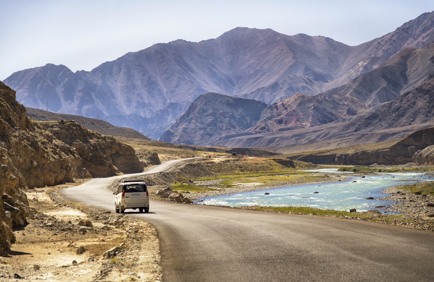 Car driving along a remote mountain road beside a glacial river in Iceland’s Highlands.