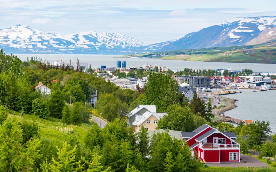 Scenic view of Akureyri town with colorful houses, Eyjafjordur fjord, and snow-capped mountains in North Iceland.