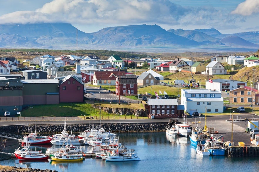 Fishing boats docked at the harbor of Stykkisholmur with colorful houses and mountains in West Iceland.