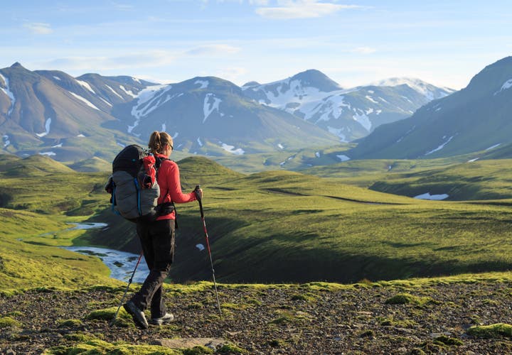 Hiker trekking in the Icelandic Highlands with views of snow-capped mountains and mossy valleys in summer.