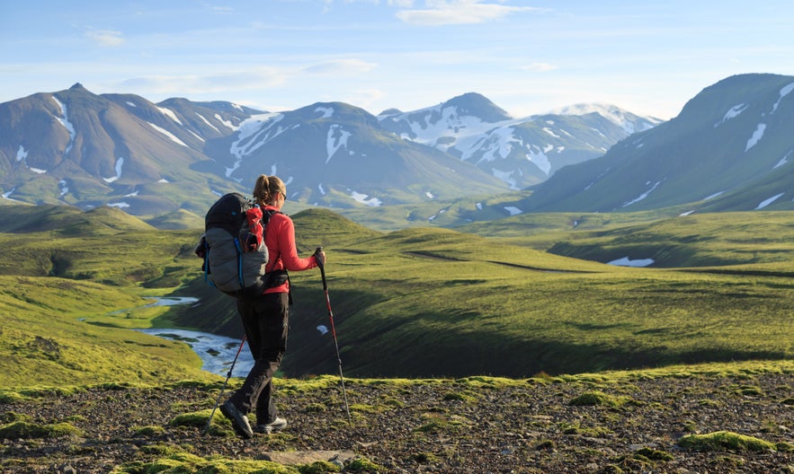 Hiker trekking in the Icelandic Highlands with views of snow-capped mountains and mossy valleys in summer.