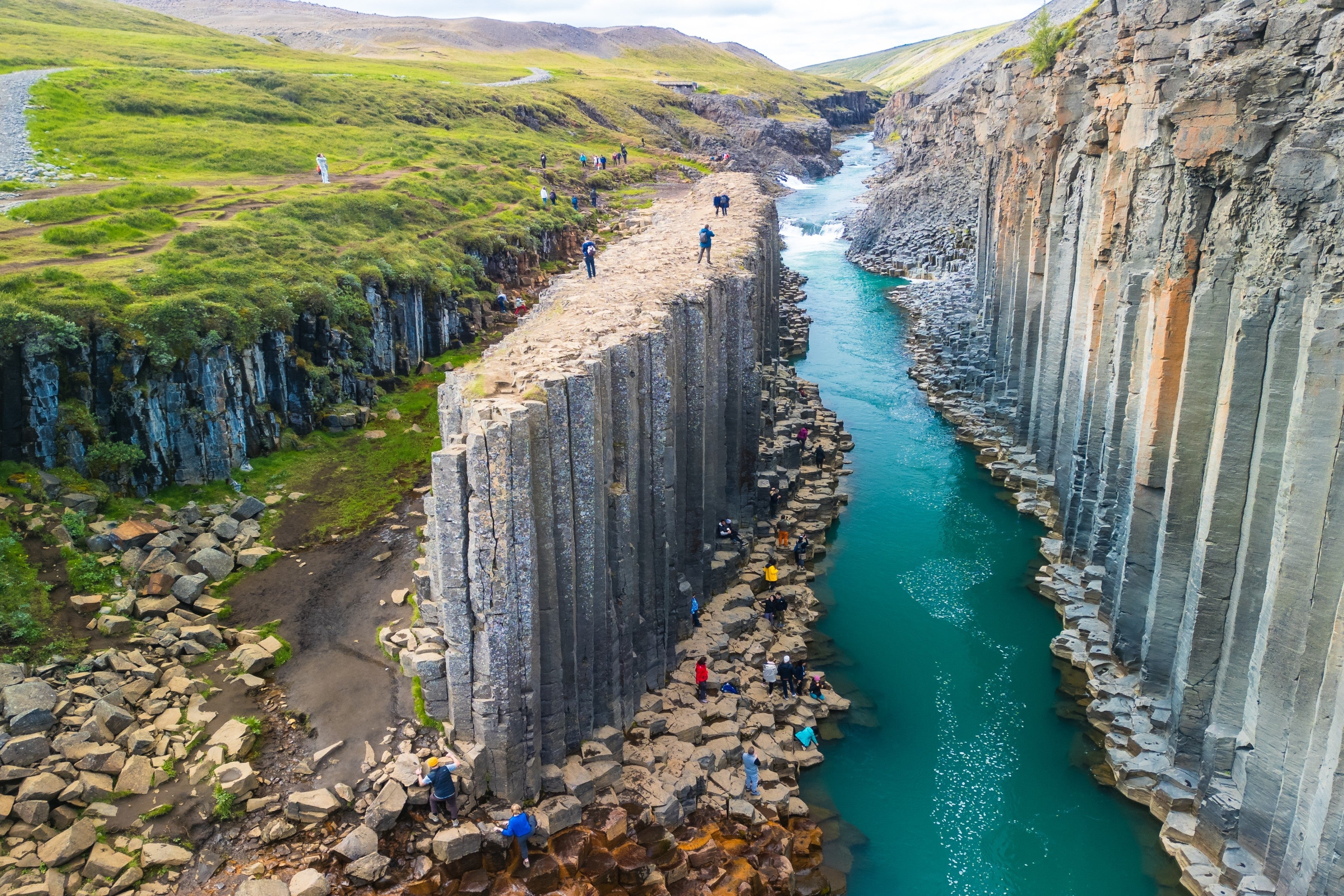 A scenic view of Studlagil Canyon in Iceland with basalt columns and a turquoise river flowing through.