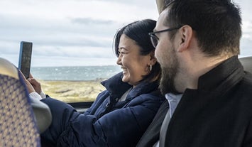 Woman and man are seen sitting in a bus smiling.