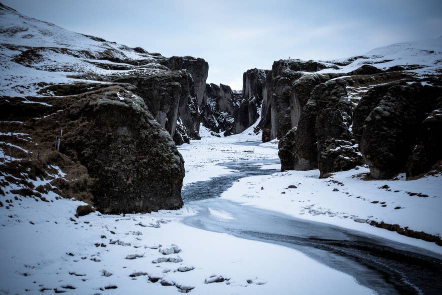 Snow-dusted Fjadrargljufur Canyon with a river winding through its steep mossy walls in winter
