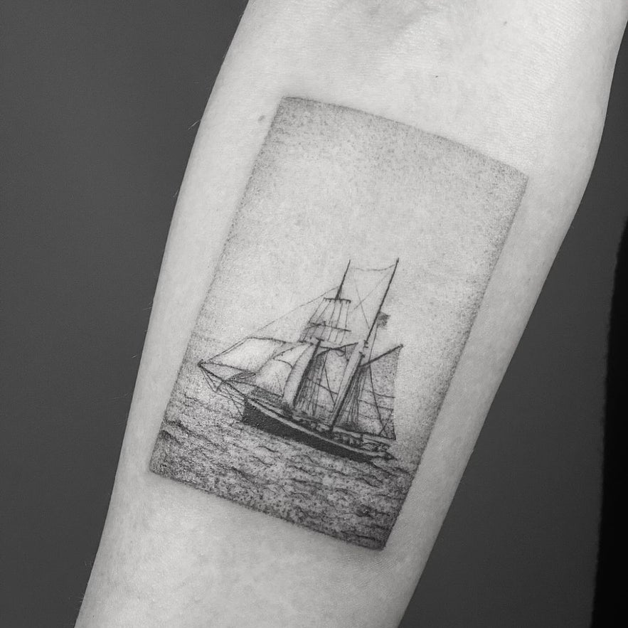 A detailed black and white tattoo of a ship navigating through water, emphasizing artistic line work and design.
