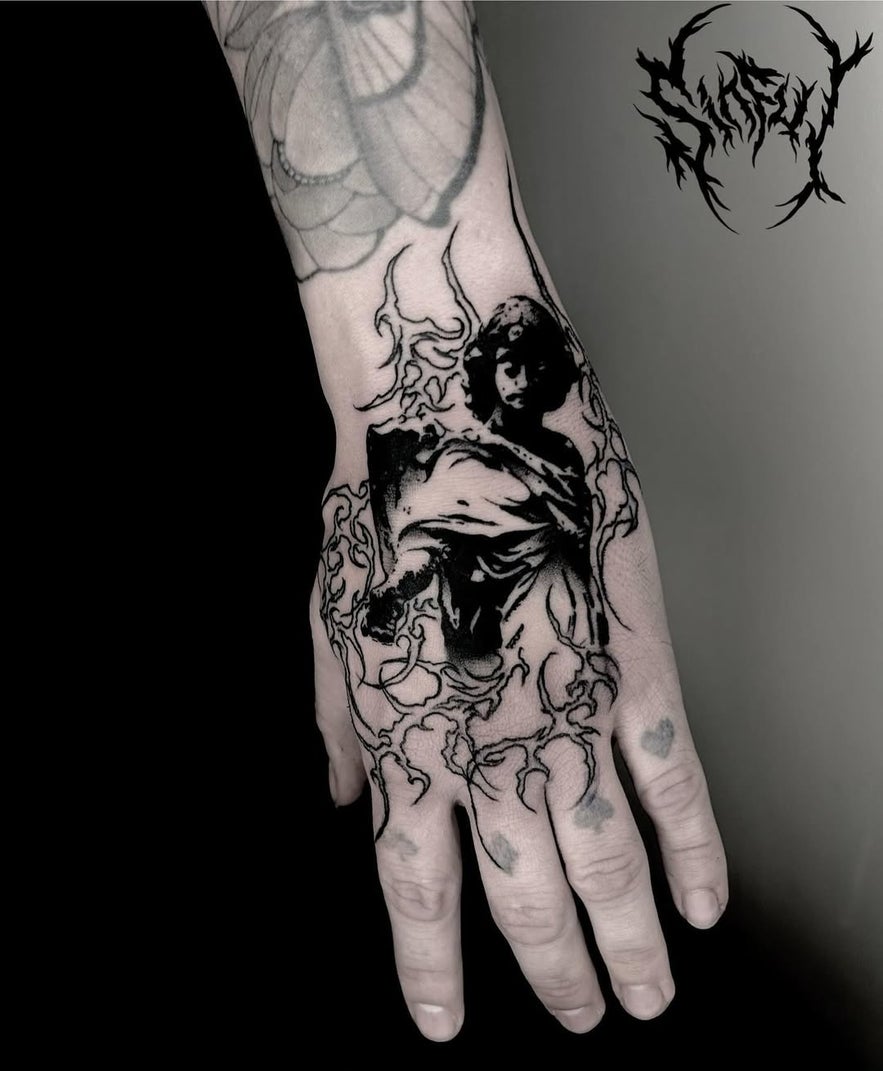 Blackwork tattoo on the hand depicting a dark, classical-style angel figure surrounded by abstract flame-like linework.
