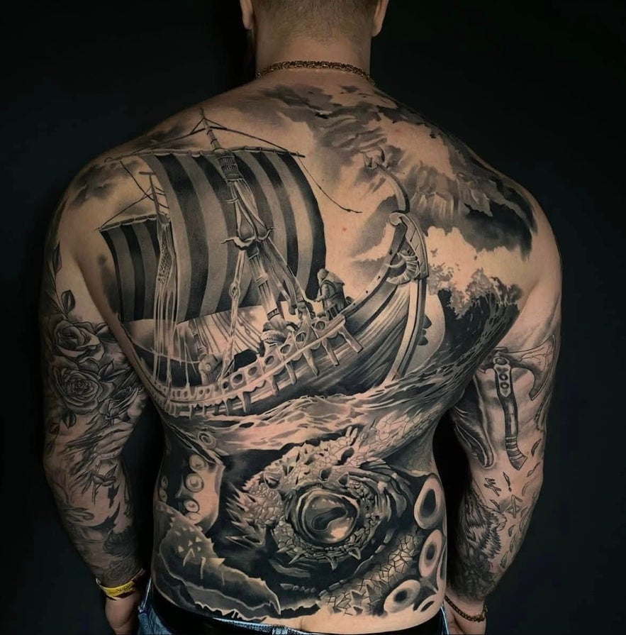 A man with a striking full-back black and grey ship tattoo, showcasing elaborate artwork and detail.
