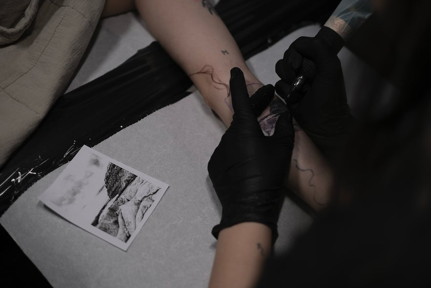 Close-up of an arm being tattooed, showing the needle in action and design in progress.