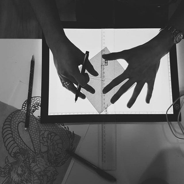 Close-up of a tattoo artist using a pen and ruler to sketch a design on paper.