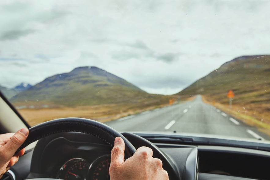 Driving along a scenic mountain road in West Iceland with open views of green hills and cloudy skies.