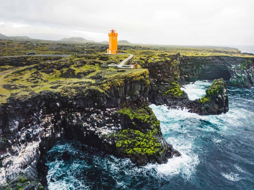 The bright orange lighthouse stands on the rugged Svortuloft Cliffs at the western tip of Iceland's Snaefellsnes Peninsula, overlooking the wild Atlantic Ocean.