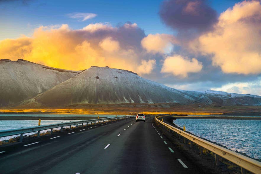 Driving toward snow-covered mountains along the coast of Hvalfjordur in West Iceland at sunset offers a breathtaking and serene experience.