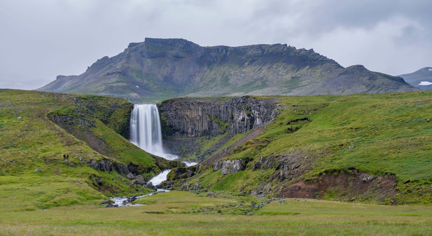 Svöðufoss waterfall on the Snæfellsnes Peninsula in Iceland, cascading over basalt columns into a lush green valley.