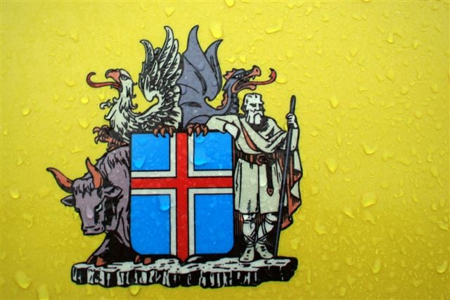 Iceland’s coat of arms shows a shield with the flag and four guardian figures: a bull, an eagle, a dragon, and a giant on a rocky base.