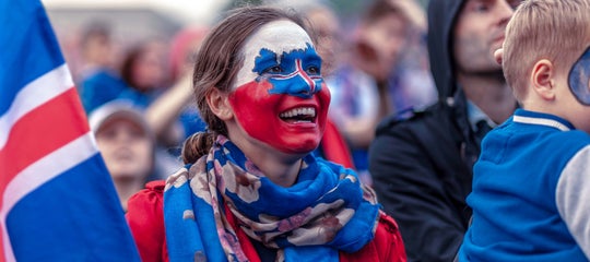 A woman with Icelandic flag face paint smiles amid a festive crowd during a public celebration in Iceland..jpg