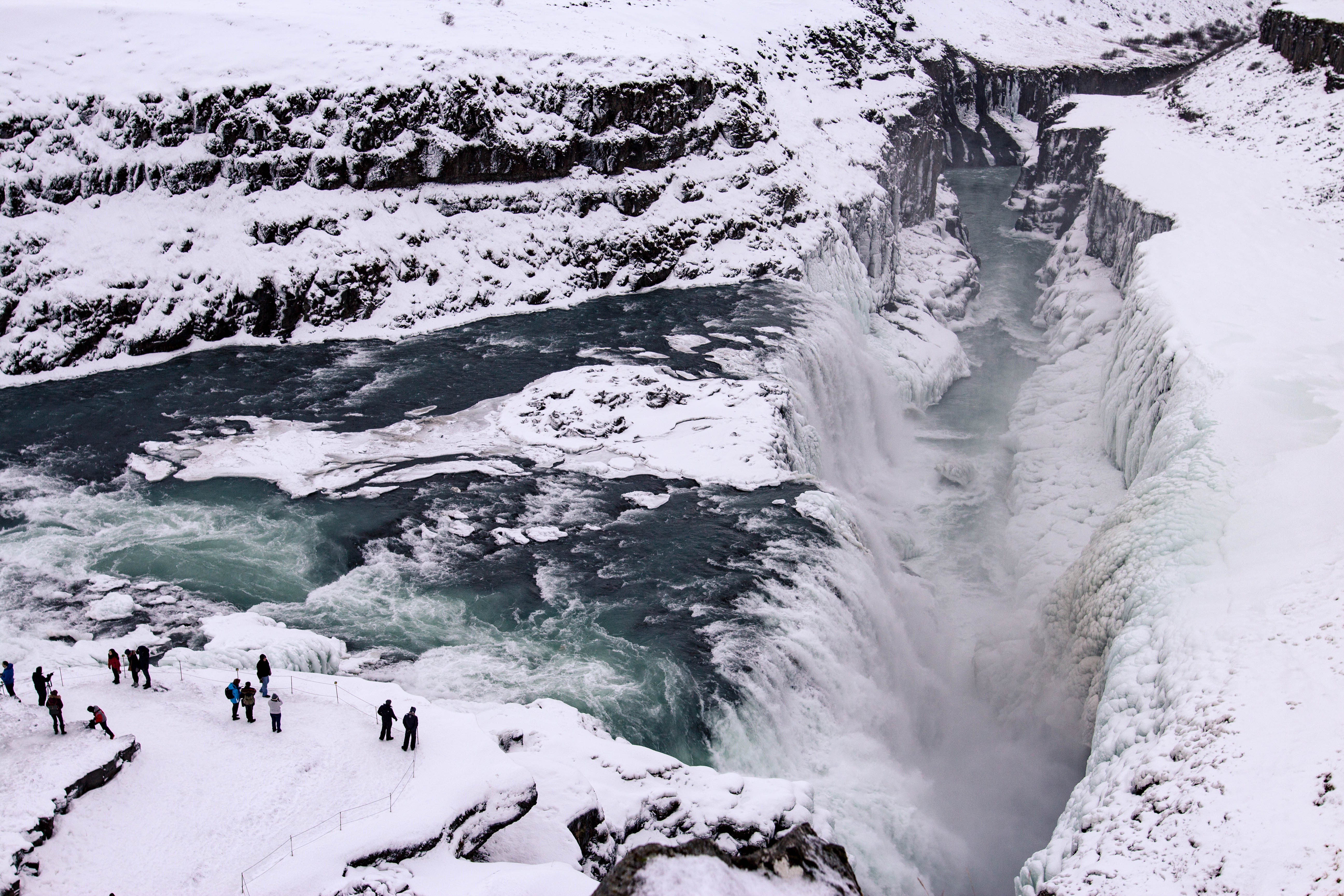 Gullfoss Waterfall partially frozen in winter, with tourists observing the powerful cascade from a nearby viewpoint.
