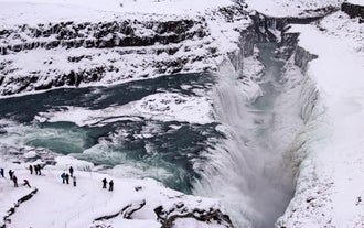 Gullfoss Waterfall partially frozen in winter, with tourists observing the powerful cascade from a nearby viewpoint.