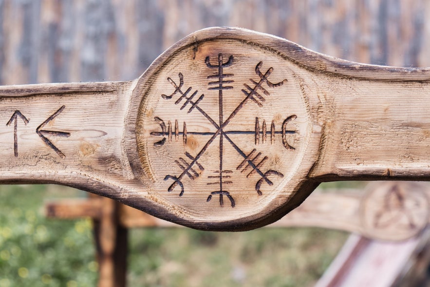 Close-up of an Icelandic magical stave, known as Aegishjalmur or Helm of Awe, carved into a wooden surface with directional runes beside it.