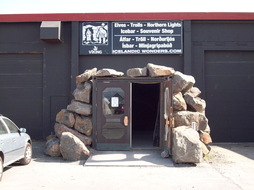 Entrance to the Ghost Centre (Draugasetrid) in Stokkseyri, Iceland, featuring a dark building facade with a cave-like doorway framed by large rocks and a sign above advertising elves, trolls, Northern Lights, and an ice bar.