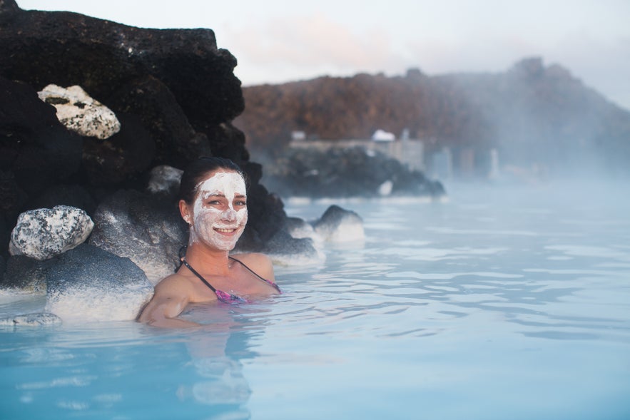 A woman with a white mud mask relaxes in the warm, milky-blue waters of Iceland's Blue Lagoon.