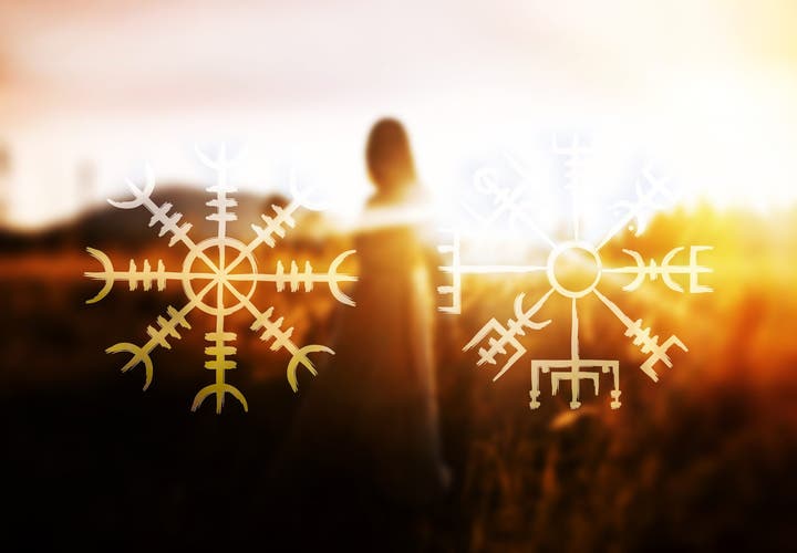 Two glowing Icelandic magical staves, Aegishjalmur on the left and Vegvisir on the right, are overlaid on a blurred image of a woman standing in a golden field at sunset.