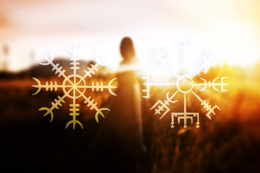 Two glowing Icelandic magical staves, Aegishjalmur on the left and Vegvisir on the right, are overlaid on a blurred image of a woman standing in a golden field at sunset.