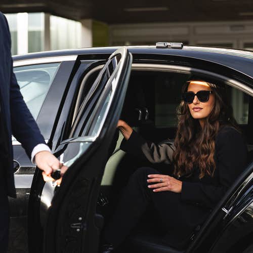 A woman steps into a private black car as a driver holds the door, showing a smooth Keflavik Airport pickup.