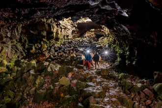 Travelers wearing hard hats with flashlights walk through the Raufarholshellir lava tunnel in Iceland.