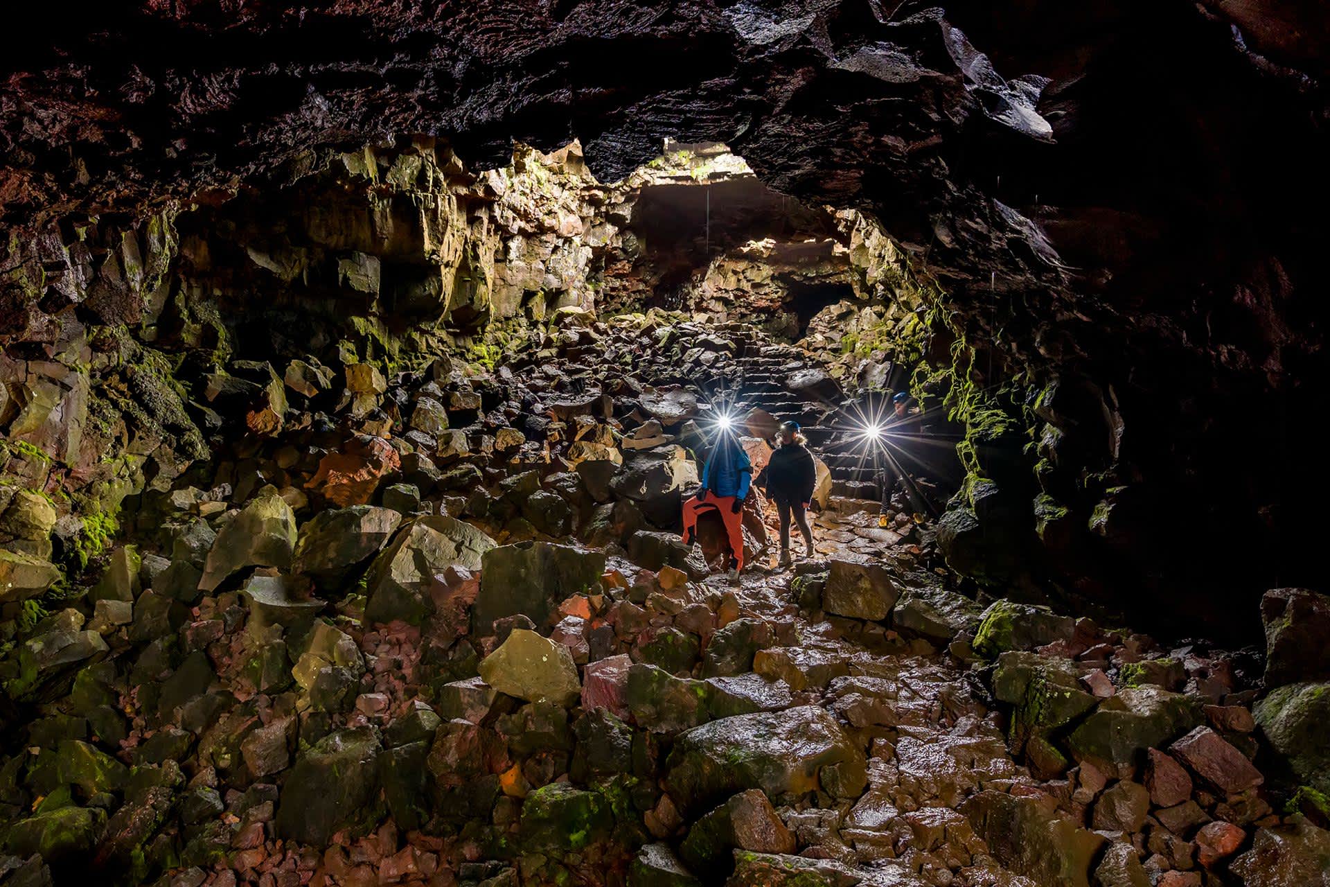 Travelers wearing hard hats with flashlights walk through the Raufarholshellir lava tunnel in Iceland.