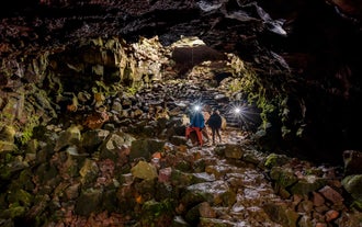 Travelers wearing hard hats with flashlights walk through the Raufarholshellir lava tunnel in Iceland.