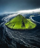 The bright green Maelifell volcano surrounded by black sands and river water.