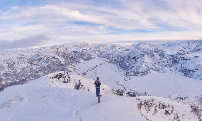 A person stands on a post and looks across the stunning Thorsmork valley covered in a blanket of snow.