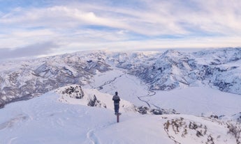 A person stands on a post and looks across the stunning Thorsmork valley covered in a blanket of snow.
