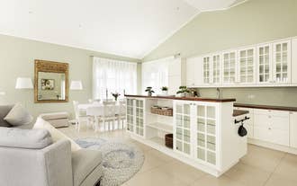 A unique island counter-slash-cabinet is the center of the kitchen with the sink, cupboards, and dining table in the background.