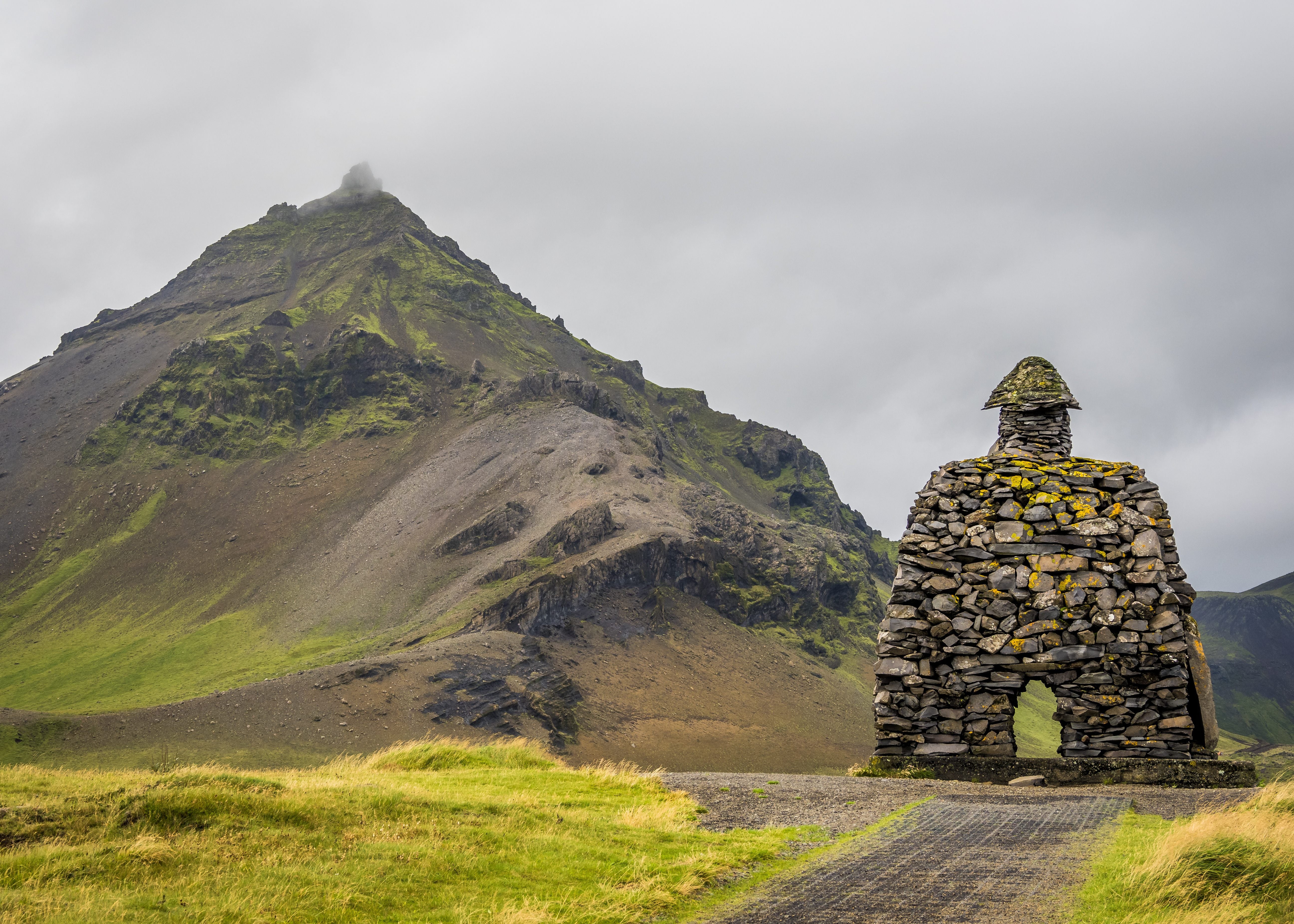 Stone statue of Bárður Snæfellsás standing in front of a dramatic moss-covered mountain on Iceland’s Snæfellsnes Peninsula under a cloudy sky.