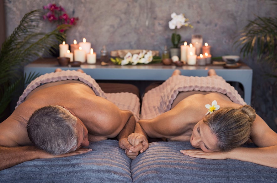 A couple enjoys a relaxing spa treatment in Reykjavik, holding hands while lying on massage tables.