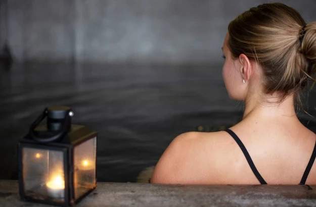 A person relaxes in the outdoor hot tub at Midgardur Spa by Center Hotels.