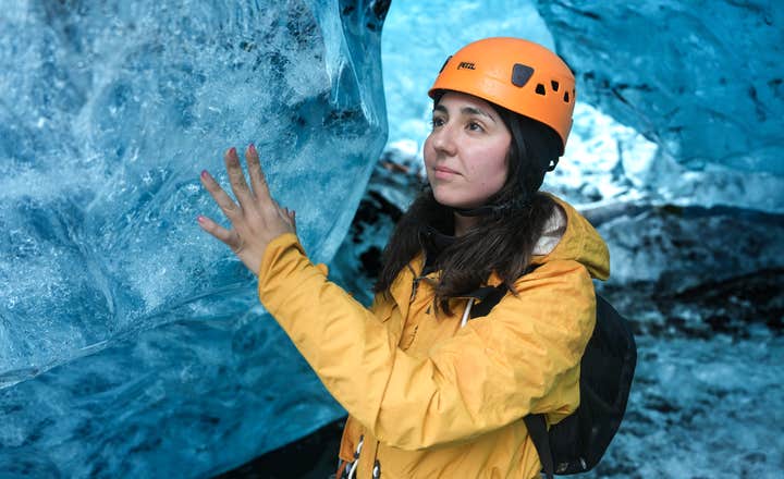 Una donna tocca delicatamente la parete liscia e ghiacciata di una grotta di ghiaccio blu in Islanda.