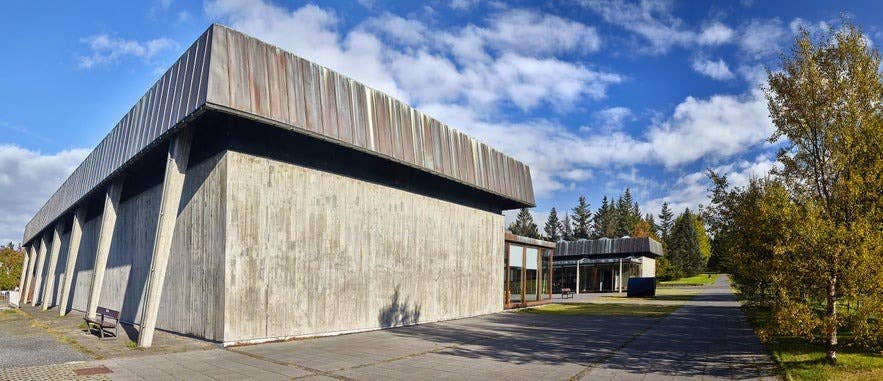 Modernist concrete exterior of Kjarvalsstaðir Art Museum in Reykjavík, surrounded by trees under a bright blue sky.