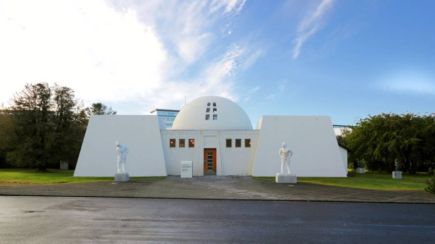 Ásmundarsafn art museum in Reykjavík, housed in a white, dome-topped building with geometric shapes and flanked by sculpted statues on a clear day.