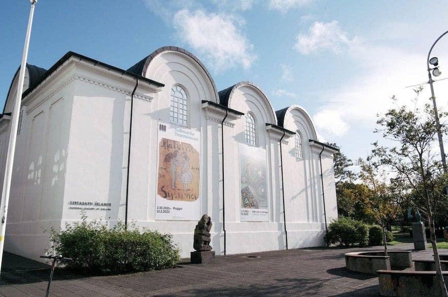 The National Gallery of Iceland in Reykjavík, a historic white building with arched windows and contemporary art banners displayed on its façade.