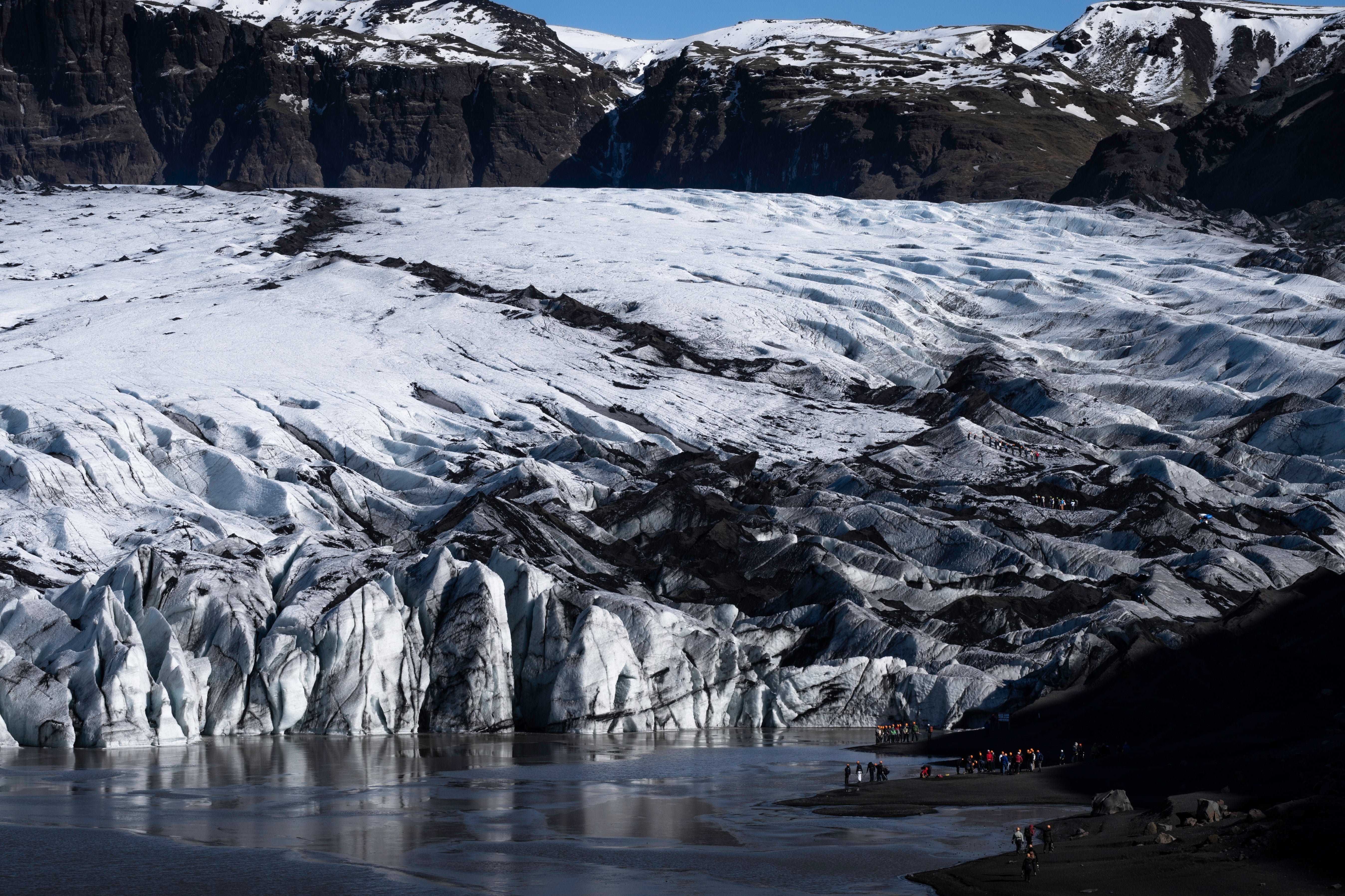 Wide view of Solheimajokull Glacier tongue with hikers exploring near its base.