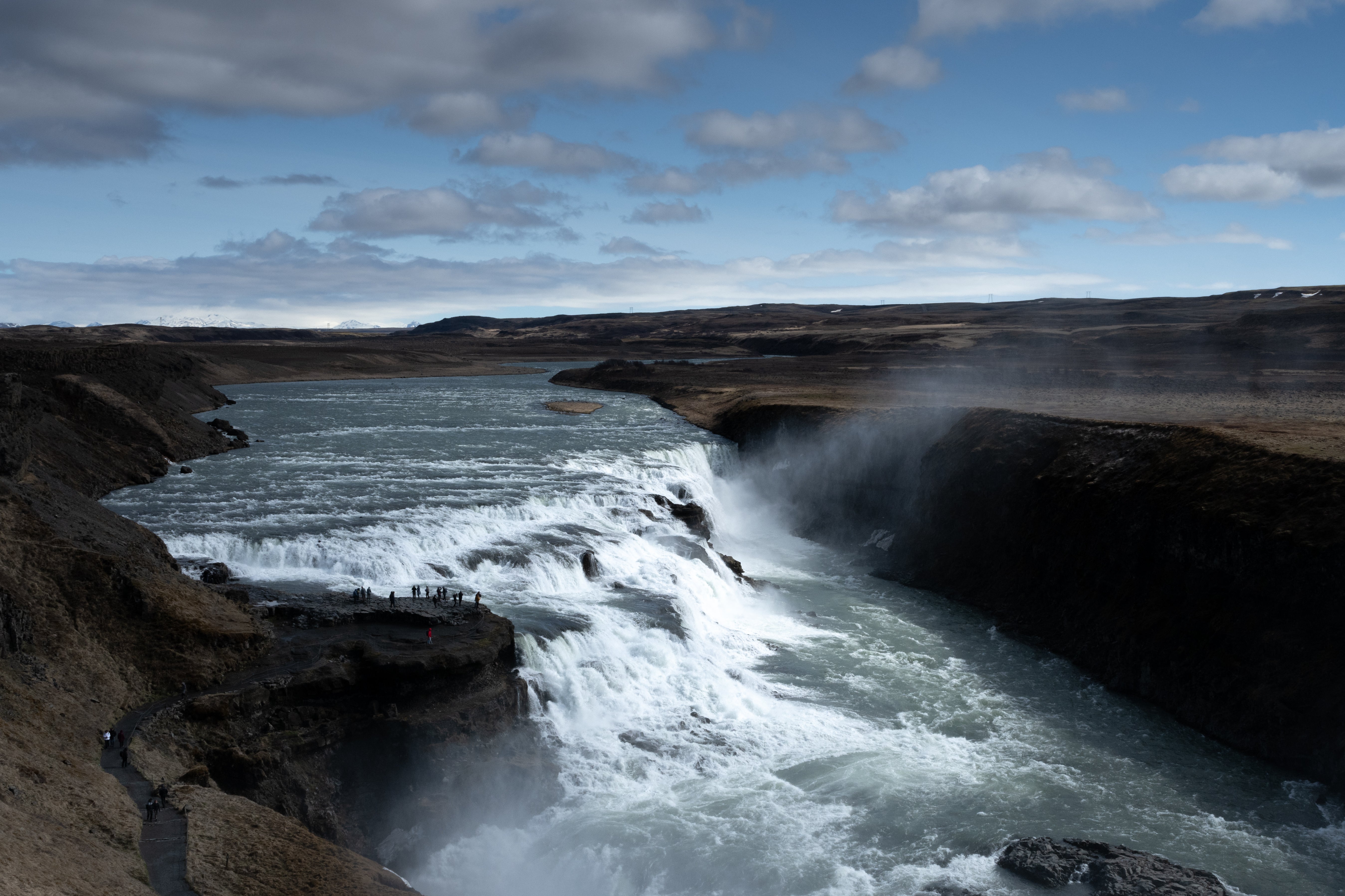 Visitors stand on a viewing platform overlooking Gullfoss Waterfall, highlighting its massive scale on a Golden Circle tour.