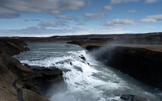 Visitors stand on a viewing platform overlooking Gullfoss Waterfall, highlighting its massive scale on a Golden Circle tour.