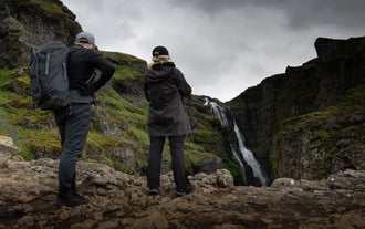 Visitors stand near the edge of the Glymur canyon to view the waterfall.