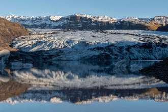 Solheimajokull Glacier with blue ice streaked with volcanic ash under clear skies.