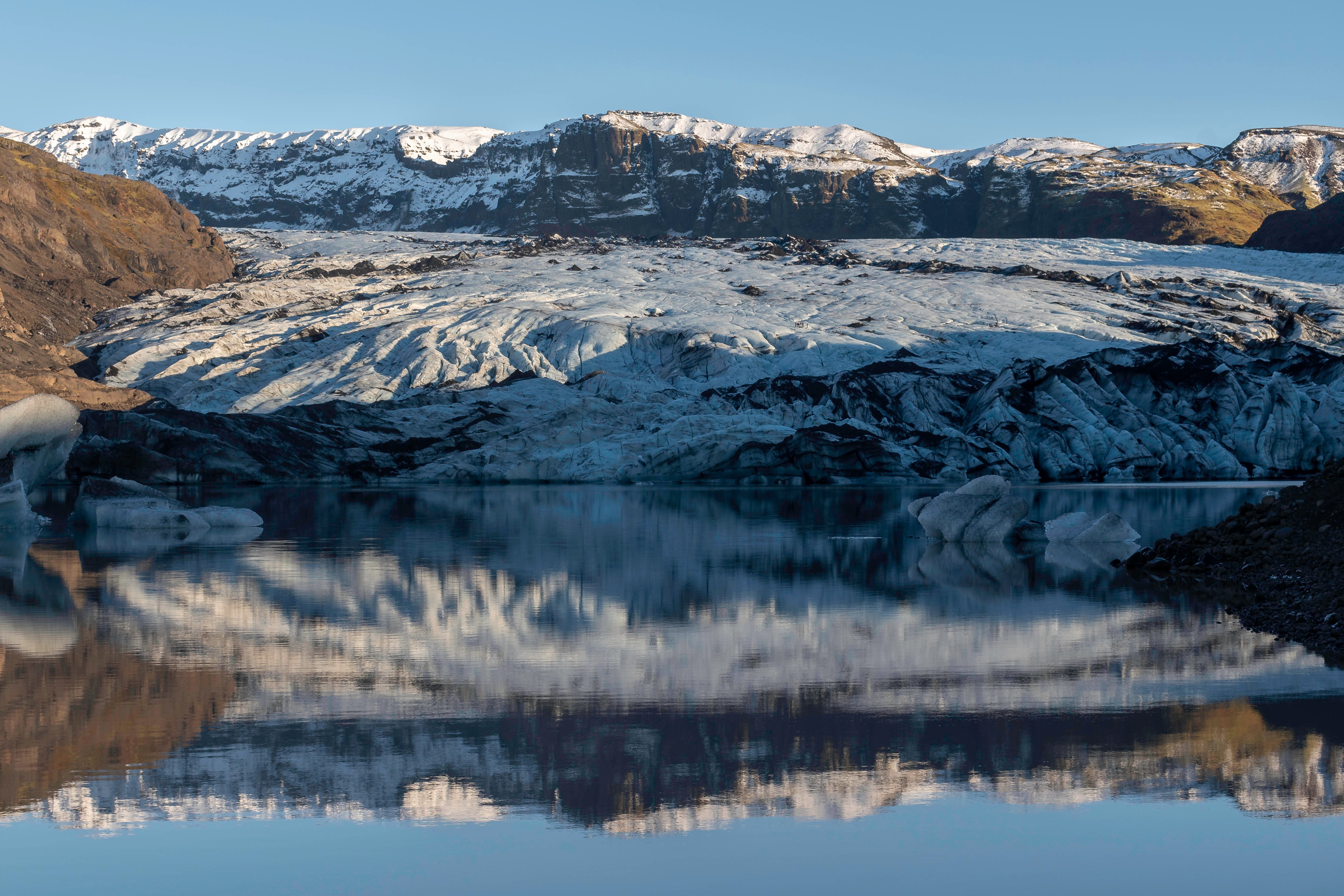 Solheimajokull Glacier with blue ice streaked with volcanic ash under clear skies.