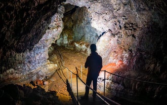 Person explores Vatnshellir Cave, standing on a lit walkway inside the volcanic lava tunnel.
