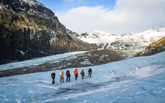 En gruppe rejsende begynder en gletsjervandring på Sólheimajökull, mens de omkringliggende bjerge byder på en betagende udsigt.