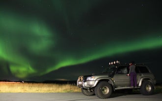Une super jeep avec une femme debout sur son rebord sous les aurores boréales en Islande.